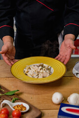 Chicken Alfredo Pasta with mushrooms on a wooden table with ingredients next to it, freshly prepared by the chef.Top view