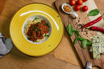Traditional italian spaghetti bolognese on a wooden table with ingredients next to it.Top view
