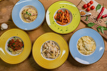 Several plates of pasta & spaghetii with different kinds of sauce over wooden background, top view. Concepts of Italian food.
