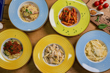 Several plates of pasta & spaghetii with different kinds of sauce over wooden background, top view. Concepts of Italian food.