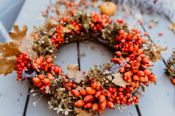 Close up photo of handmade colorful floral autumn door wreath made of colorful rosehip berries, rowan, dry flowers and oak leaves. Fall flower decoration workshop.