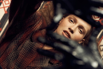 stylish curly girl in a vintage checkered jacket, leather gloves, she is lying on the mat of a loft studio, looking at the camera through folded  frame arms - 386609714