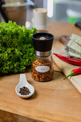Chili in a glass container and peppercorns on a wooden table