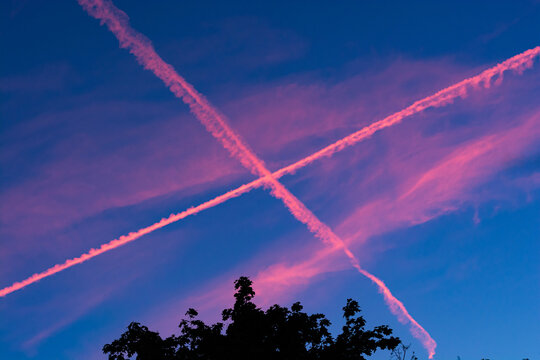 Pink chemtrails on dark blue sky in sunset
