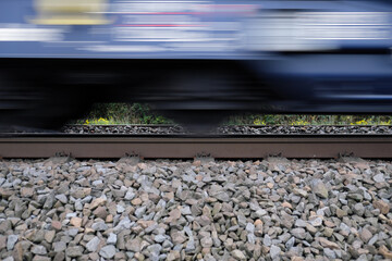 Gleisbett mit Schotter und Gleis und Ausschnitt von vorbeifahrendem Güterzug mit Bewegungsunschärfe - Stockfoto