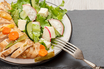 Plate with meat, vegetable salad with cheese, cucumber and radish on stone board.