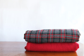 A stack of folded knitted sweaters on a wooden table and a white background, close up.
