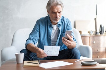 Senior man in couch reading message, using smartphone.