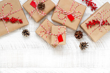 Christmas presents wrapped in craft paper and pine cones on the white wooden background. New year flat lay. Gift boxes decorated with striped baker's twine string. Top view, copy space.