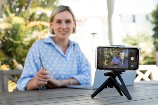 Young blurred business woman recording the video on smartphone and working at the laptop outdoors. Happy smile blogger. Selective focus