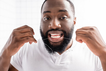 portrait of afro-american man using dental floss and looking at camera