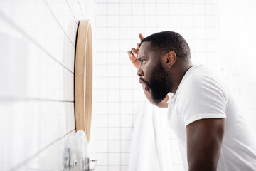 side view of afro-american man looking at wrinkles in mirror