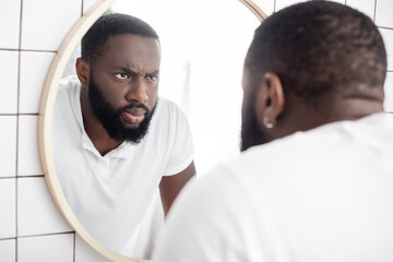 serious afro-american man looking at reflection in mirror