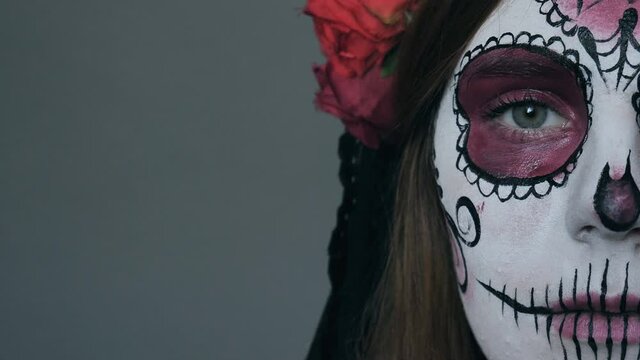 Halloween makeup. Half face of a woman in the image of death (Santa Muerte or sugar Mexican skull) on a gray background.