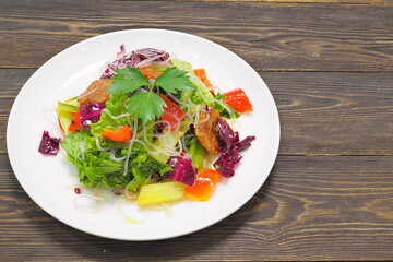 Chinese cuisine. Cabbage salad with celery and starch noodles on a white plate on a wooden table.