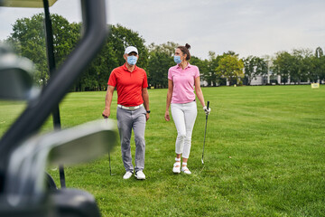 Two golfers in protective masks crossing the golf course