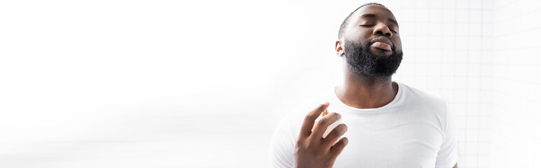 Obraz premium panoramic shot of afro-american man in white t-shirt using perfume