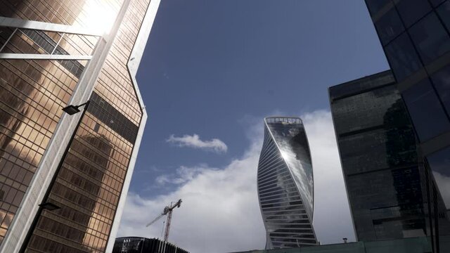 Bottom view of the glass skyscrapers of the business district against blue cloudy sky. Action. Beautiful commercial office buildings, concept of modern architecture.