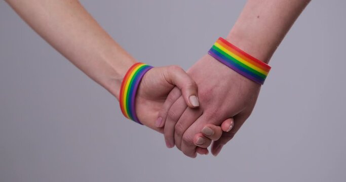 Male couple wearing gay pride rainbow awareness wristbands holding hands over white background