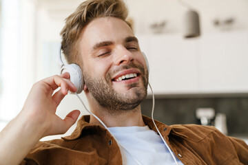 Handsome happy guy smiling while listening music with headphones