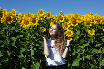 A girl of European appearance with long blond hair stands in sunflowers.