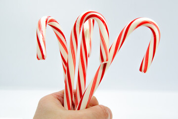 Hand holds a bundle of striped candy canes on a white background. Christmas mood, gifts and...