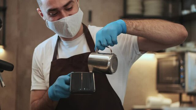 A cropped view of handsome young guy barista is making coffee behind the counter during quarantine indoors