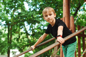 Fototapeta premium Happy boy having fun at summer park. Adventure park for kids. Boy in a treehouse outdoors.