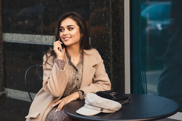 Fototapeta na wymiar Seductive girl at coffee shop outside. Technology and lifestyle. Fashionable girl with mobile phone sitting at cafe outdoors.