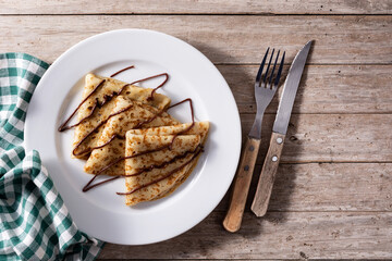 Sweet crepes with chocolate on wooden table.	