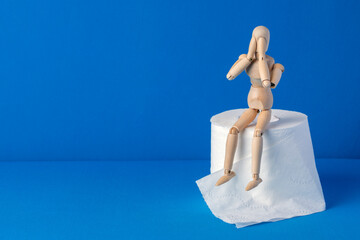 The little wooden man sits on toilet paper and covers his face with his hands in shame and pain....