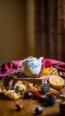 White teapot surronded by autumn related stuff like leaves, chestnuts or cones, fall warming beverage, cozy and hygge autumn home concept 