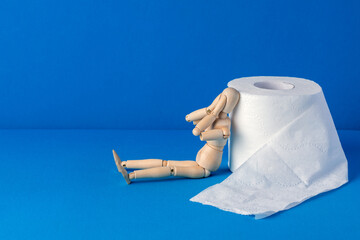 The little wooden man sits next to toilet paper and covers his face with his hands in shame and...