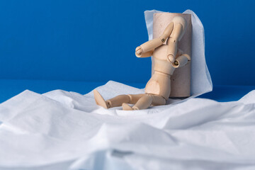 The little wooden man sits next to toilet paper and covers his face with his hands in shame and...