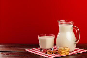 Glass pitcher and cup of milk against red background