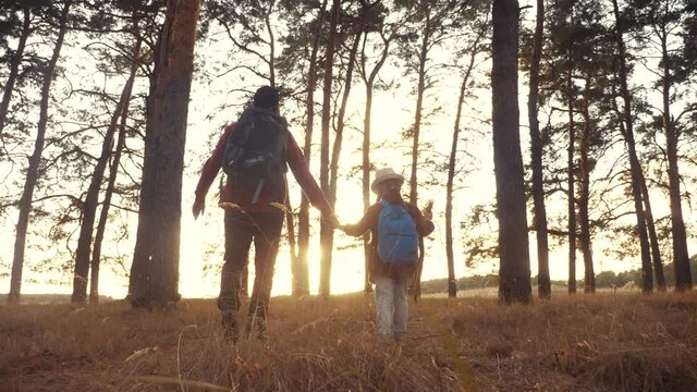 happy family with backpacks go on a trip through the park. travel kid dream adventure concept. dad and tourist kid daughter go hiking in the park with pine trees. happy family dream about adventure