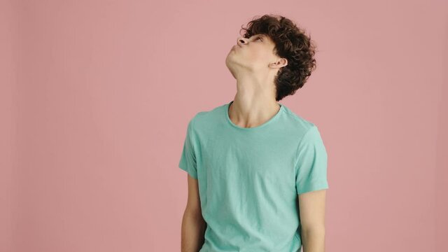 A bored sleepy young man is yawning standing isolated over pink background