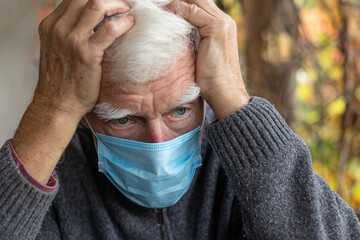 Senior grey-haired man covering his head with hands, sitting alone on the porch with the medical...