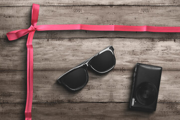 Eyeglasses and camera with red ribbon on wooden background
