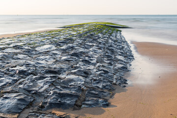 Lateral side of a stone breakwater still wet and shining during ebb tide.