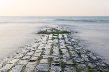 A wet stone breakwater is half submerged in blurred waters.