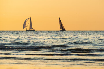 Two sailing boats go in opposite directions under a golden sky.