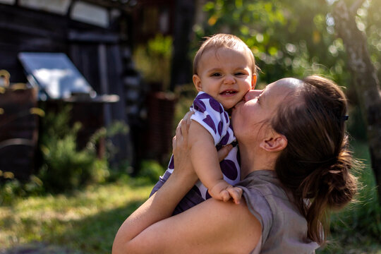 Photo of a young Caucasian mother playing with her daughter, outdoors.Cheerful mother holding baby girl on the beautiful sunny day in nature.Mother and daughter having fun.Mom and baby love.Copy space
