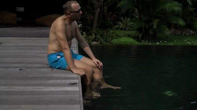 Sad, depressed man sitting at the edge of  swimming pool