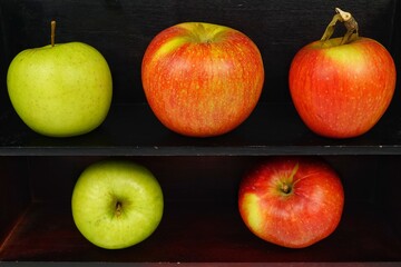 Red and green ripe apples lie on wooden shelves, background