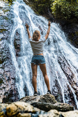 Young caucasian slender woman tourist in casual clothes and sneakers stands on a rock and look at waterfall 