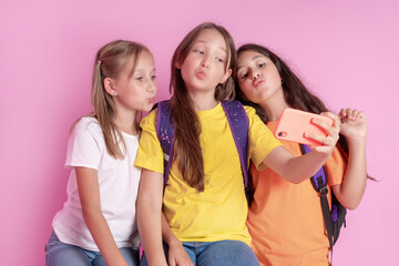 Three teen girls smiling and shoots a video on a pink background. Selfies