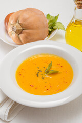 Pumpkin soup and organic pumpkins on white table.