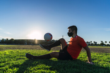 Chico joven con mascarilla por el covid 19 preparandose y jugando al futbol