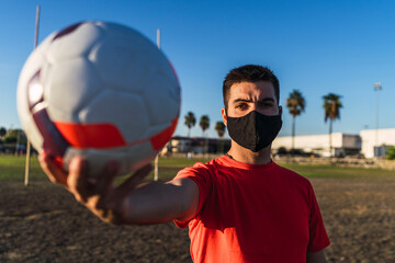 Chico joven con mascarilla por el covid 19 preparandose y jugando al futbol
